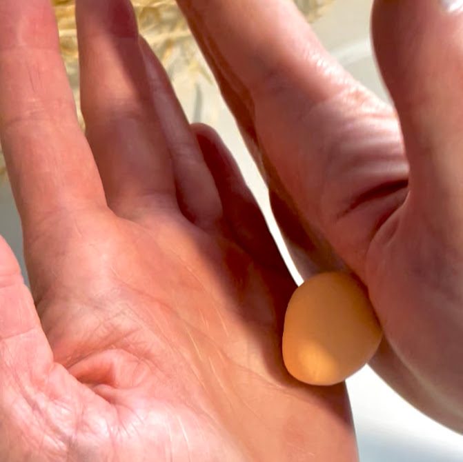 Mains en train de rouler un morceau de pâte orange pastel dans les paumes pour former une boule lisse et bien ronde, étape de préparation des coques de macarons.