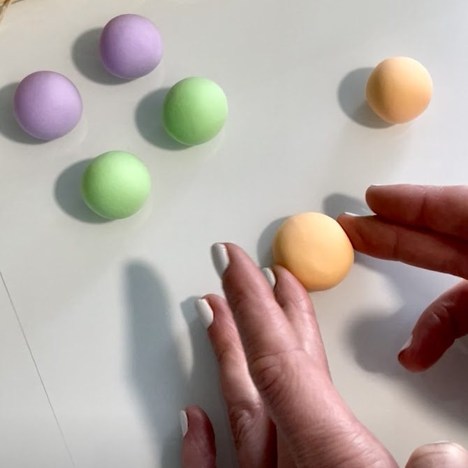 Mains en train d’aplatir doucement une boule de pâte orange pastel pour lui donner la forme d’une coque de macaron.