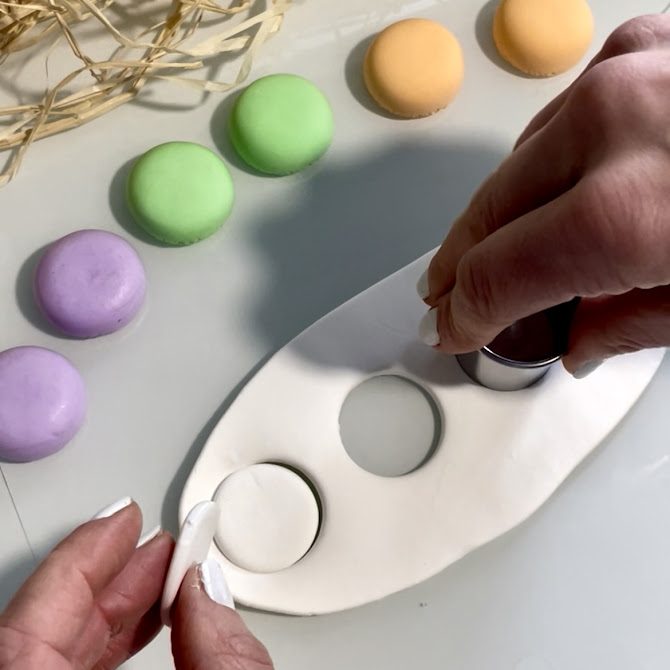 Mains découpant des cercles dans une plaque de pâte de silk clay étalée à environ 2 mm d’épaisseur à l’aide d’un emporte-pièce.