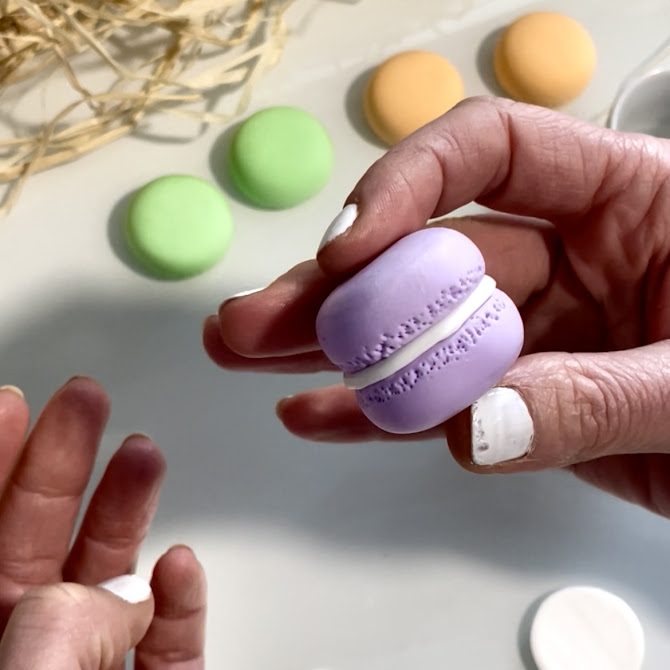 Mains présentant un macaron violet en foam clay assemblé, montrant les deux coques réunies avec une finition soignée.