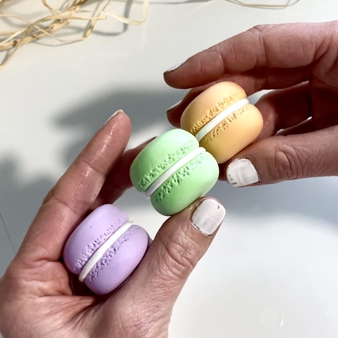 Mains présentant trois macarons en foam clay — orange, vert et violet — entièrement assemblés et terminés, avec une finition réaliste et soignée.