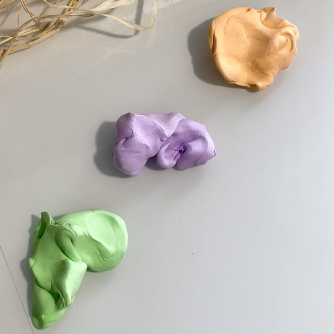 Trois morceaux de pâte colorée uniformes en orange pastel, violet pastel et vert pastel, obtenues après mélange complet de la Silk Clay blanche avec la Foam Clay colorée.