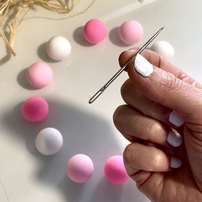 Mains montrant une grosse aihuille et 12 boules de foam clay rondes derrière sur la table