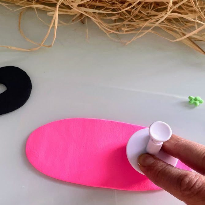 Main utilisant un emporte-pièce avec poussoir sur la plaque de foam clay rose.