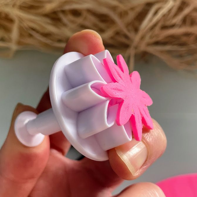 Main appuyant sur la tige de l’emporte-pièce pour faire sortir la fleur rose.