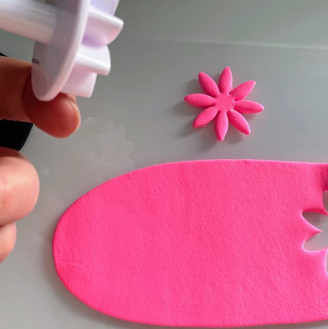 Fleur en foam clay rose posée sur la table, plaque rose avec une empreinte de fleur à côté.