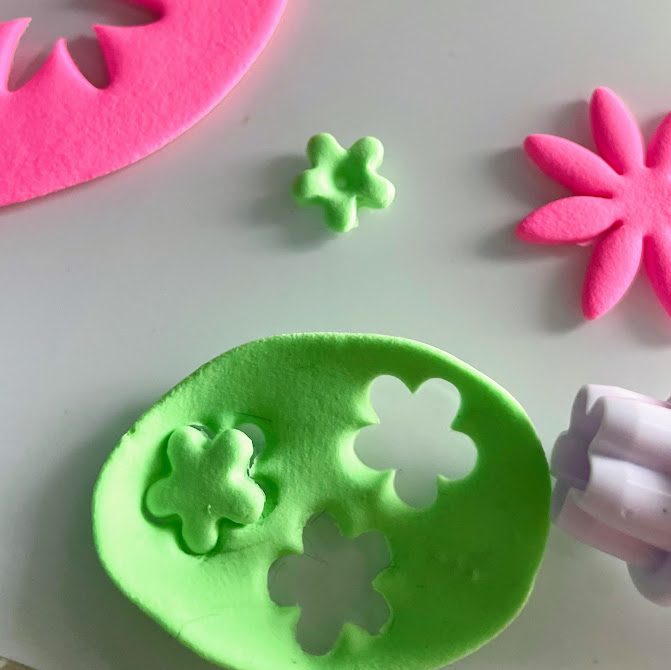 Plaques de foam clay verte et rose avec des fleurs découpées, une fleur verte posée à côté.