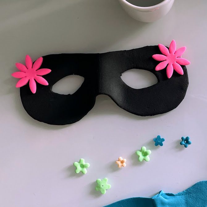 Masque noir avec fleurs décoratives disposées autour : grosses roses, petites vertes et mini bleues.