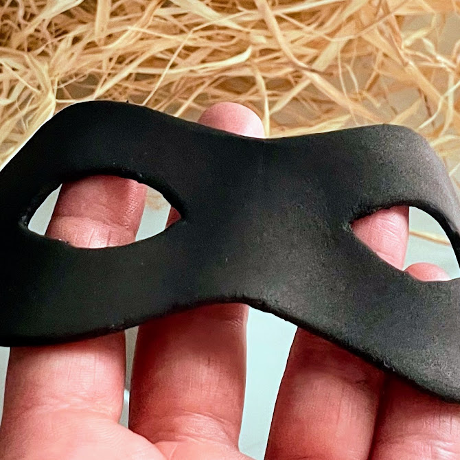 Mains tenant le masque en foam clay noire moulé pour suivre la forme du visage, avec relief pour le nez.