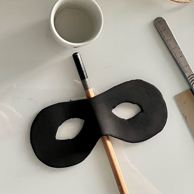 Masque en foam clay posé sur la table, maintenu en forme avec un crayon sous le nez.